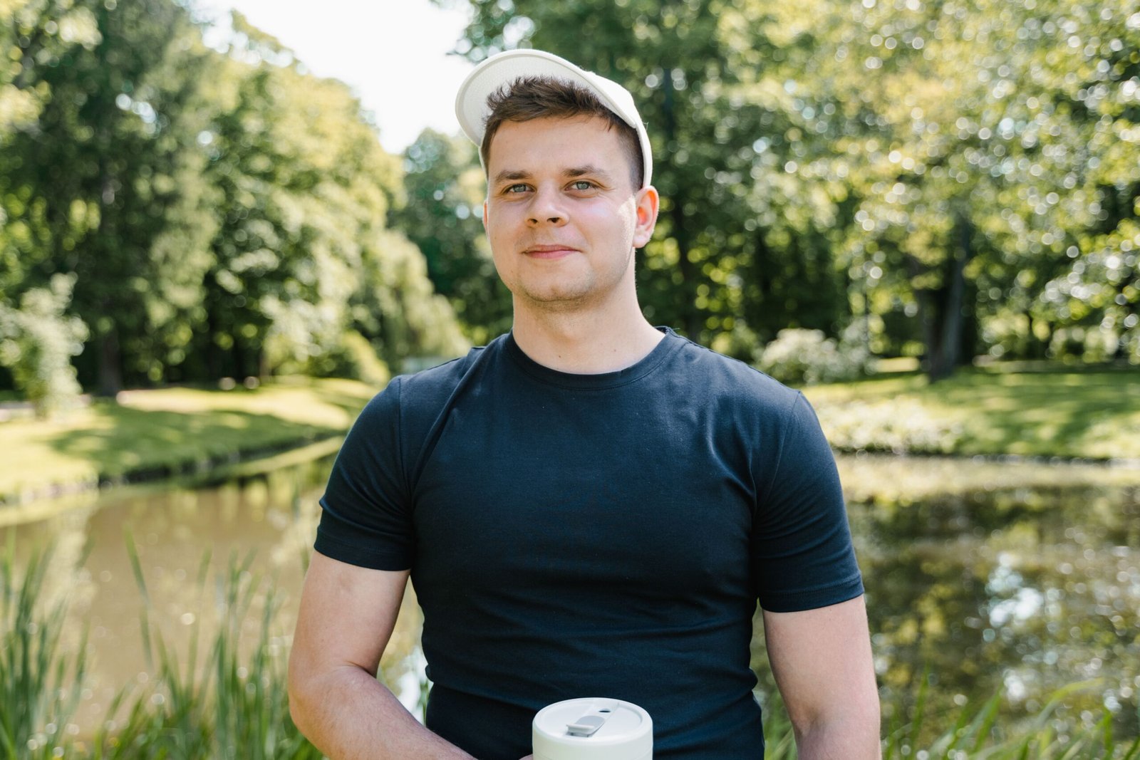 Smiling young man in a park on a sunny day, wearing a black shirt and cap.